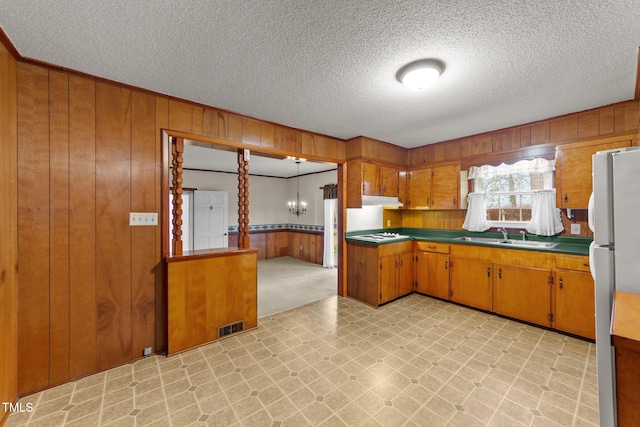 kitchen featuring sink, wood walls, a textured ceiling, decorative light fixtures, and white appliances