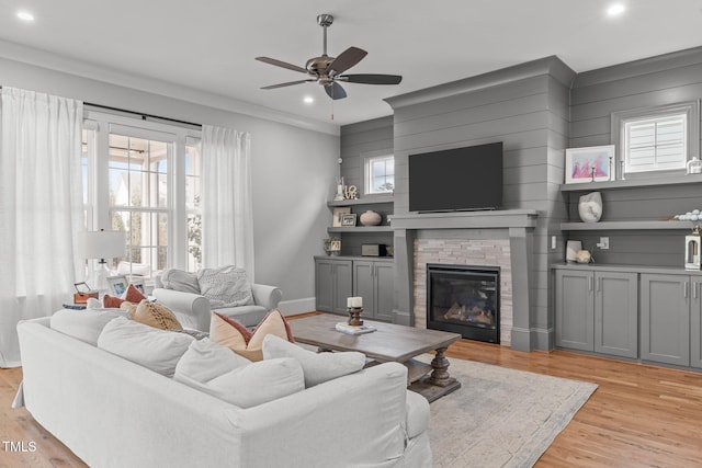 living room with light hardwood / wood-style floors, ceiling fan, crown molding, and a fireplace