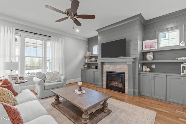 living room featuring ceiling fan, light hardwood / wood-style flooring, and a stone fireplace