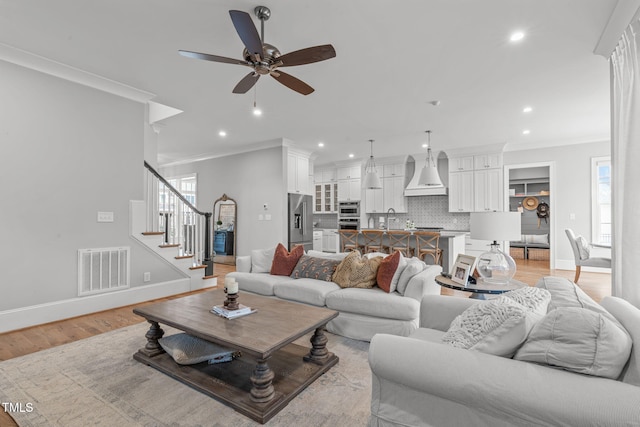 living room featuring ceiling fan, light hardwood / wood-style floors, crown molding, and sink