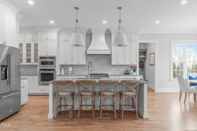 kitchen featuring stainless steel appliances, a kitchen island with sink, custom exhaust hood, and pendant lighting