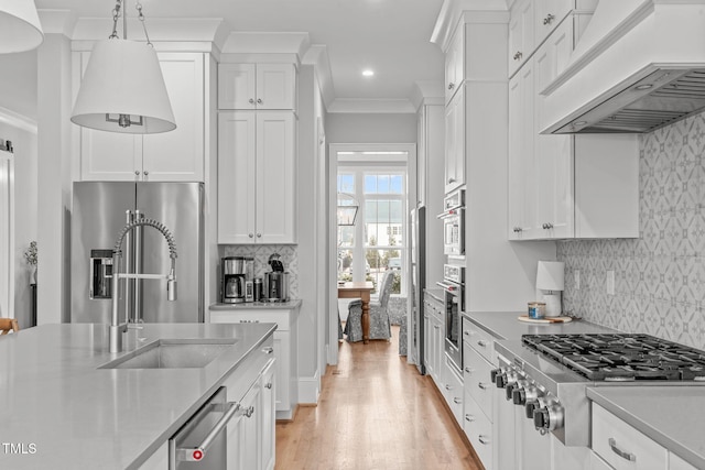 kitchen with stainless steel appliances, crown molding, custom range hood, white cabinets, and decorative light fixtures