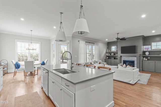 kitchen featuring sink, a fireplace, an island with sink, ceiling fan with notable chandelier, and pendant lighting