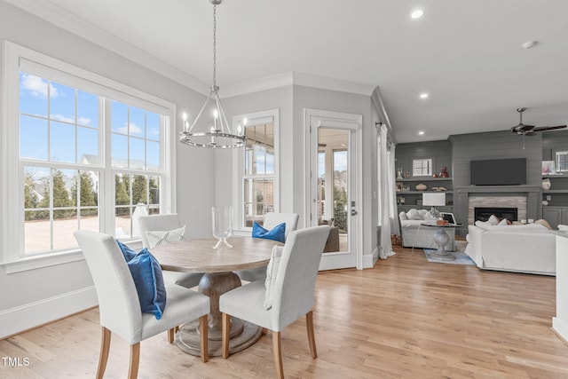 dining area with light hardwood / wood-style floors, ornamental molding, a fireplace, built in features, and ceiling fan with notable chandelier