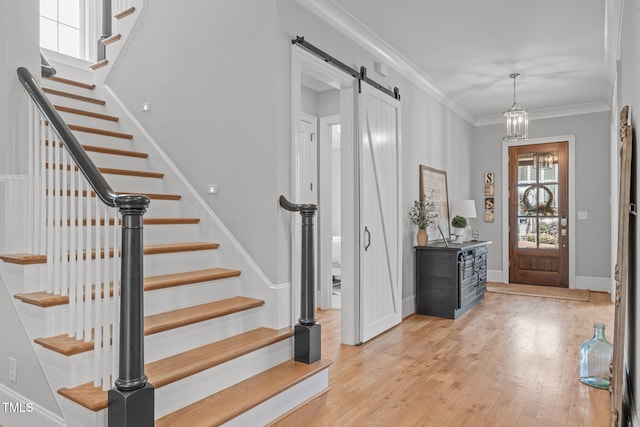 entryway featuring an inviting chandelier, ornamental molding, a barn door, and light hardwood / wood-style flooring