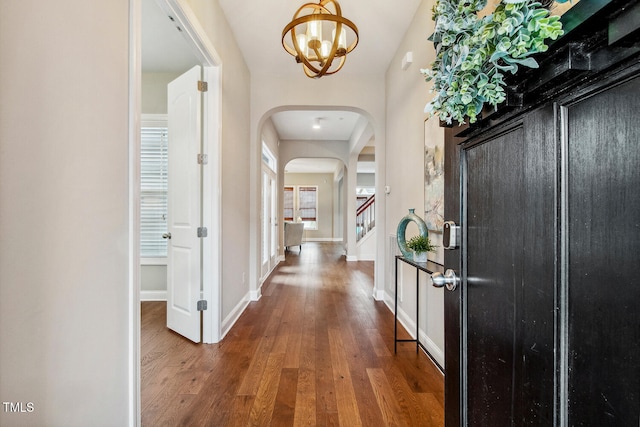 foyer entrance featuring arched walkways, wood finished floors, a chandelier, baseboards, and stairs