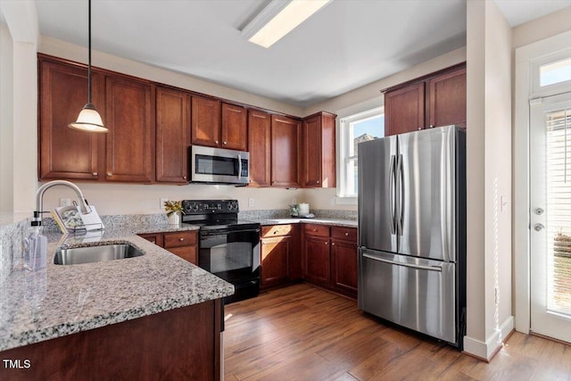 kitchen with appliances with stainless steel finishes, light stone counters, decorative light fixtures, sink, and dark hardwood / wood-style floors