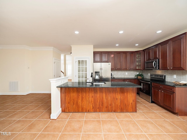 kitchen with tasteful backsplash, an island with sink, appliances with stainless steel finishes, and light tile patterned floors