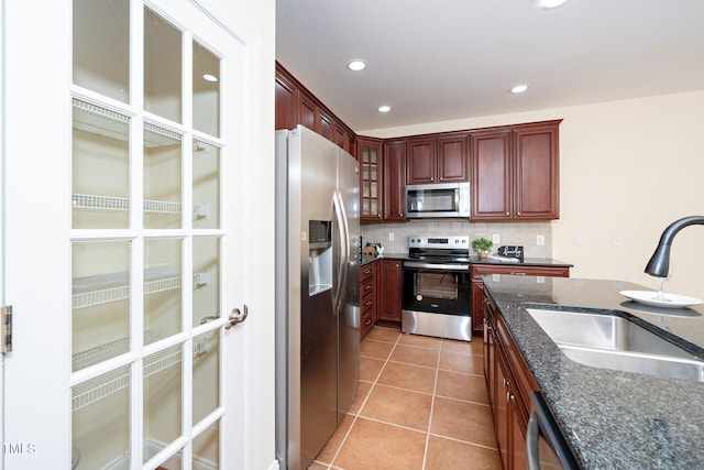 kitchen with light tile patterned flooring, sink, appliances with stainless steel finishes, dark stone counters, and decorative backsplash