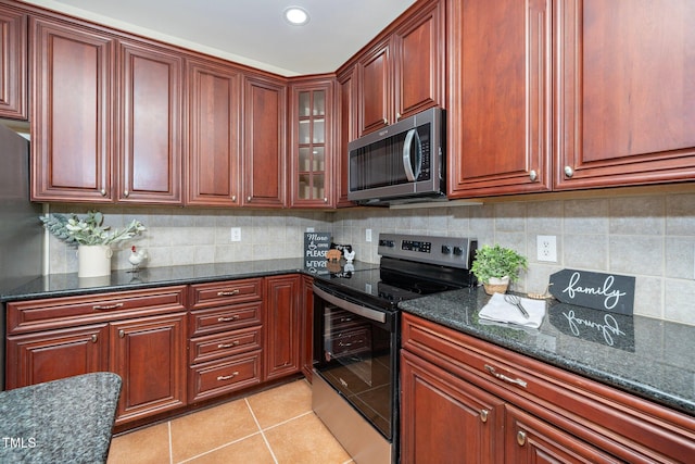 kitchen featuring dark stone countertops, backsplash, light tile patterned flooring, and appliances with stainless steel finishes