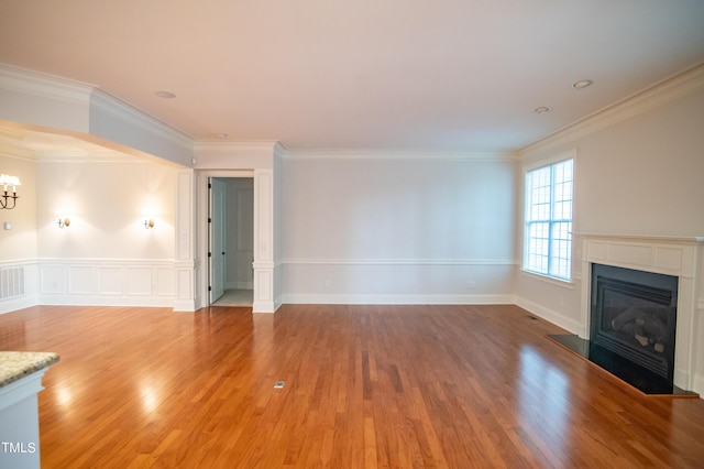 unfurnished living room with light wood-style flooring, a glass covered fireplace, ornamental molding, and a chandelier