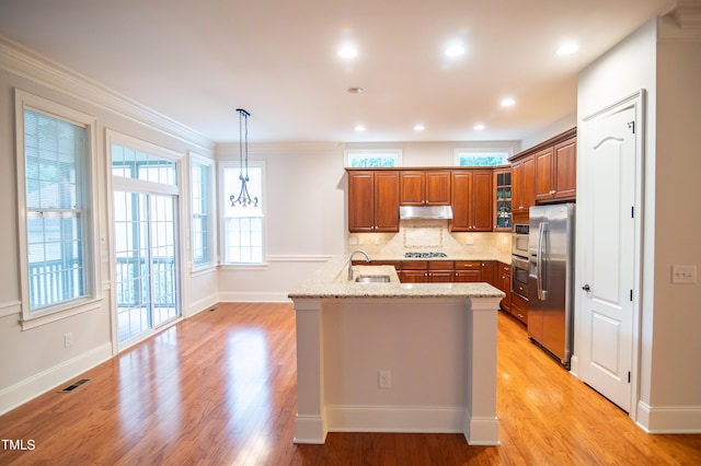 kitchen with tasteful backsplash, light stone countertops, under cabinet range hood, appliances with stainless steel finishes, and brown cabinetry