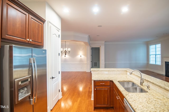 kitchen with a sink, stainless steel appliances, light stone counters, and light wood-style flooring