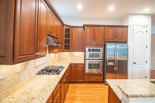 kitchen with light stone counters, light wood-style floors, under cabinet range hood, and stainless steel appliances