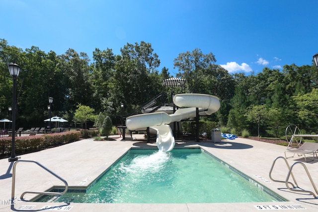 pool with a patio area, a water slide, and fence