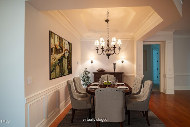 dining space featuring wood finished floors, crown molding, a raised ceiling, a decorative wall, and a chandelier