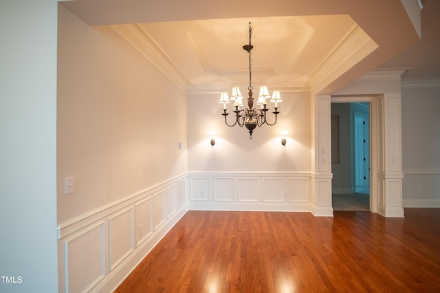 unfurnished dining area with wood finished floors, an inviting chandelier, crown molding, a raised ceiling, and a decorative wall