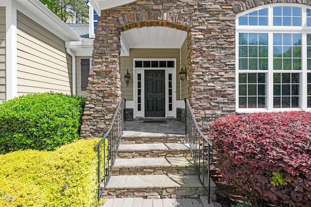doorway to property with stone siding and a shingled roof