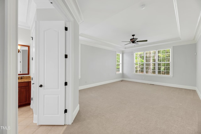empty room with a raised ceiling, crown molding, ceiling fan, and baseboards