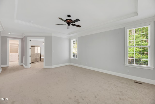 empty room with ornamental molding, a tray ceiling, and light colored carpet