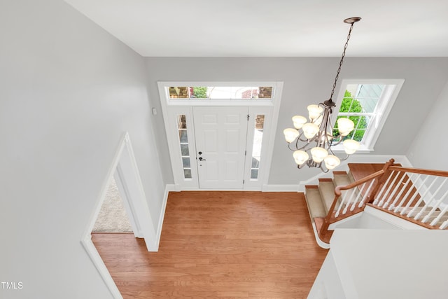 entryway with stairs, a notable chandelier, light wood-type flooring, and baseboards