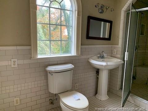 bathroom featuring tile patterned flooring, toilet, a shower with shower door, and tile walls