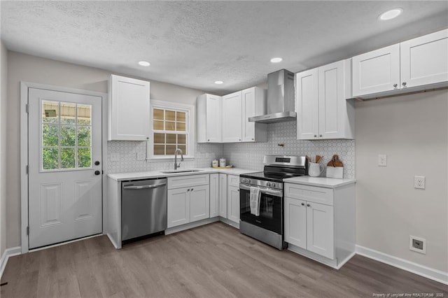 kitchen featuring white cabinetry, sink, wall chimney range hood, appliances with stainless steel finishes, and light wood-type flooring