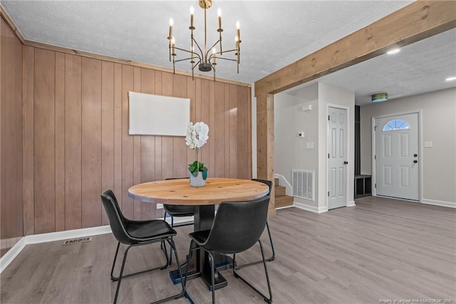 dining area with wood walls, an inviting chandelier, a textured ceiling, and hardwood / wood-style flooring