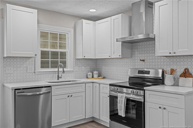 kitchen featuring white cabinets, wall chimney range hood, sink, decorative backsplash, and appliances with stainless steel finishes