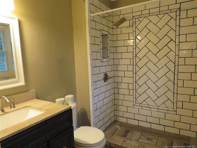 bathroom featuring a tile shower, vanity, and toilet