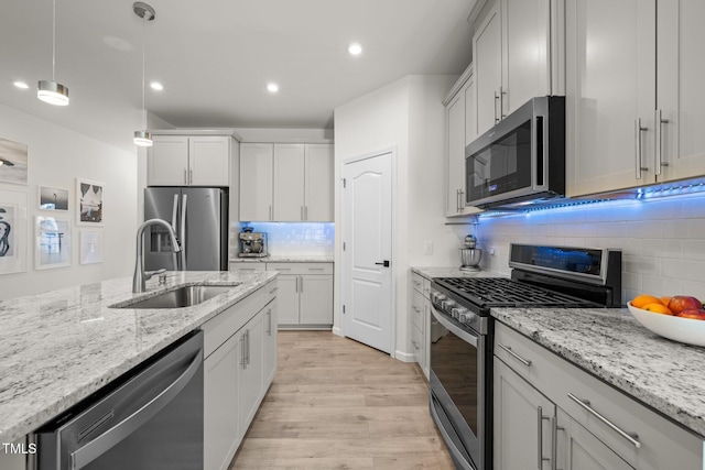 kitchen with light wood finished floors, decorative light fixtures, light stone counters, appliances with stainless steel finishes, and a sink