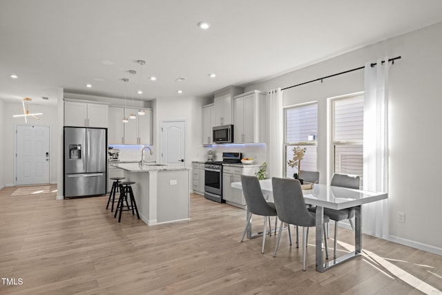 kitchen featuring a center island with sink, recessed lighting, stainless steel appliances, light wood-style floors, and a kitchen bar