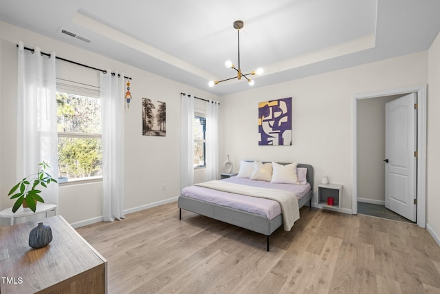 bedroom featuring light wood-type flooring, visible vents, and a raised ceiling