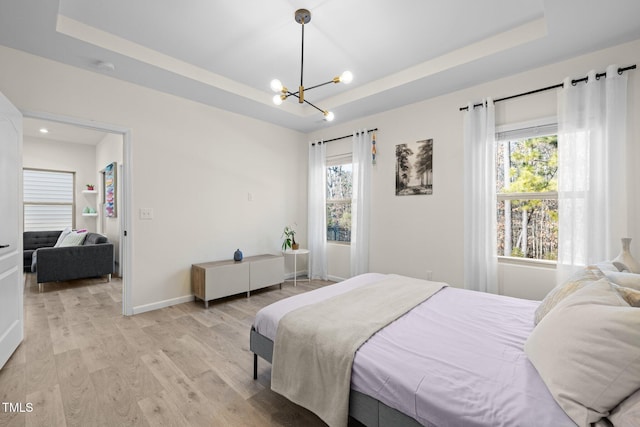 bedroom with an inviting chandelier, a tray ceiling, light wood-style floors, and baseboards