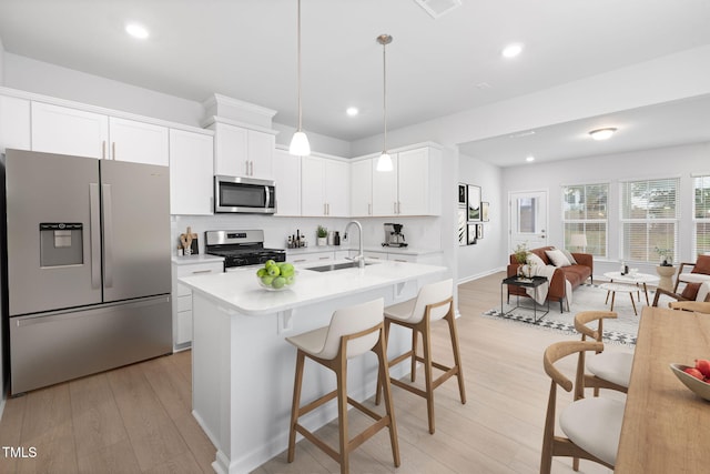 kitchen featuring stainless steel appliances, a kitchen island with sink, sink, pendant lighting, and white cabinetry