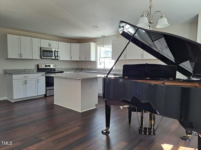 kitchen featuring white cabinets, hanging light fixtures, a kitchen island, light stone counters, and stainless steel appliances