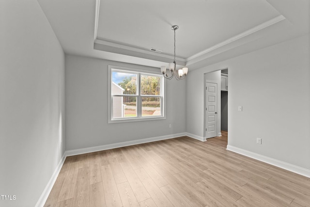 empty room with a tray ceiling, ornamental molding, a chandelier, and light wood-type flooring