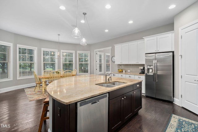 kitchen featuring a kitchen island with sink, sink, appliances with stainless steel finishes, decorative light fixtures, and white cabinetry