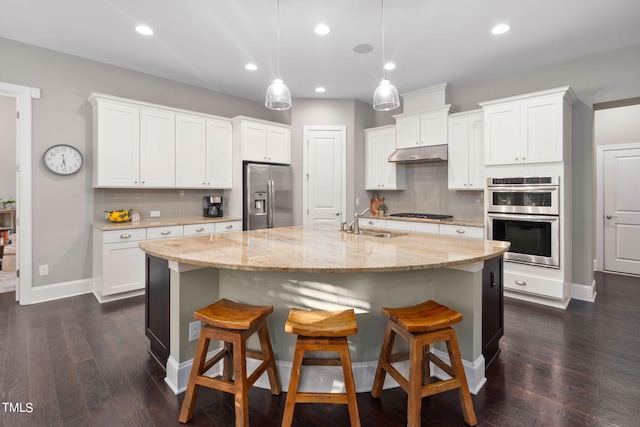 kitchen featuring decorative backsplash, appliances with stainless steel finishes, pendant lighting, a center island with sink, and white cabinetry