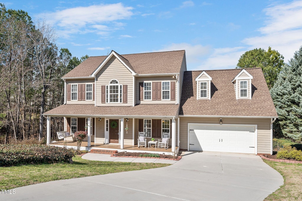 colonial home featuring a porch, an attached garage, a shingled roof, driveway, and a front yard