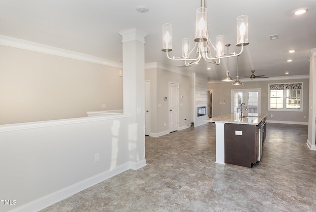 kitchen with decorative light fixtures, ornate columns, an island with sink, ceiling fan with notable chandelier, and dark brown cabinets