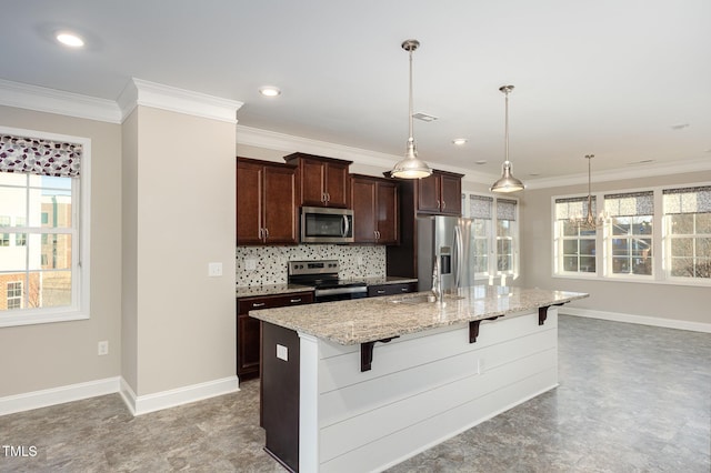 kitchen featuring light stone countertops, decorative light fixtures, stainless steel appliances, a kitchen bar, and a kitchen island with sink