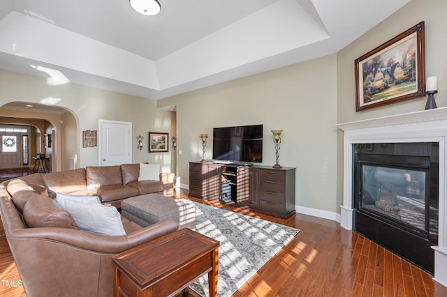 living room featuring dark hardwood / wood-style floors, a tile fireplace, and a tray ceiling