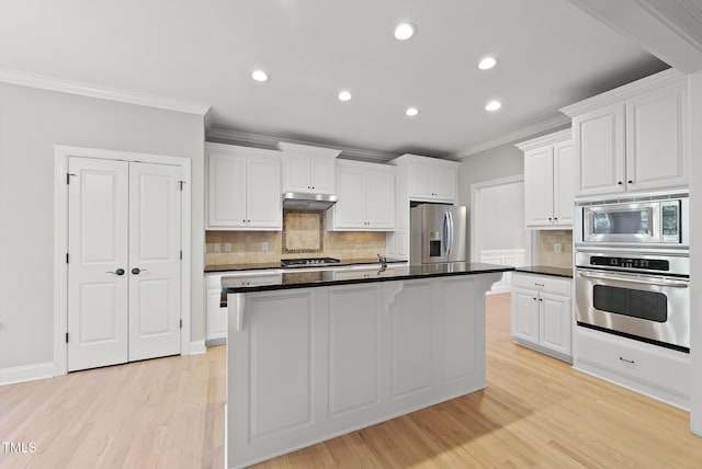 kitchen featuring white cabinets, stainless steel appliances, tasteful backsplash, and an island with sink