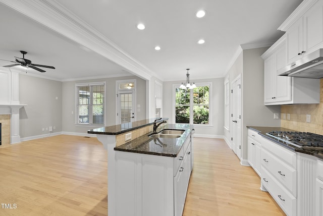 kitchen with ornamental molding, stainless steel gas cooktop, sink, dark stone countertops, and white cabinetry