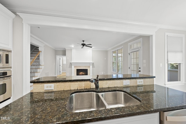 kitchen with appliances with stainless steel finishes, ornamental molding, dark stone counters, sink, and white cabinetry