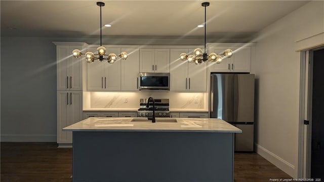 kitchen featuring pendant lighting, a kitchen island with sink, sink, light stone countertops, and appliances with stainless steel finishes