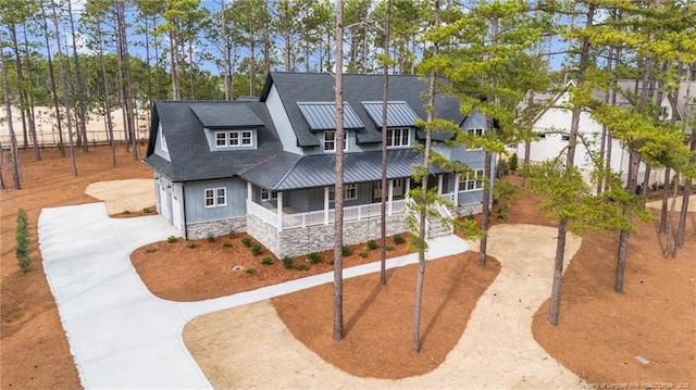 view of front of home featuring metal roof, covered porch, concrete driveway, stone siding, and a standing seam roof