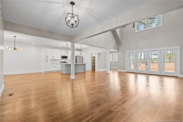 unfurnished living room with light wood-type flooring, an inviting chandelier, and a healthy amount of sunlight