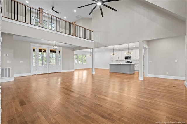 unfurnished living room with ceiling fan with notable chandelier, light wood-type flooring, visible vents, and baseboards